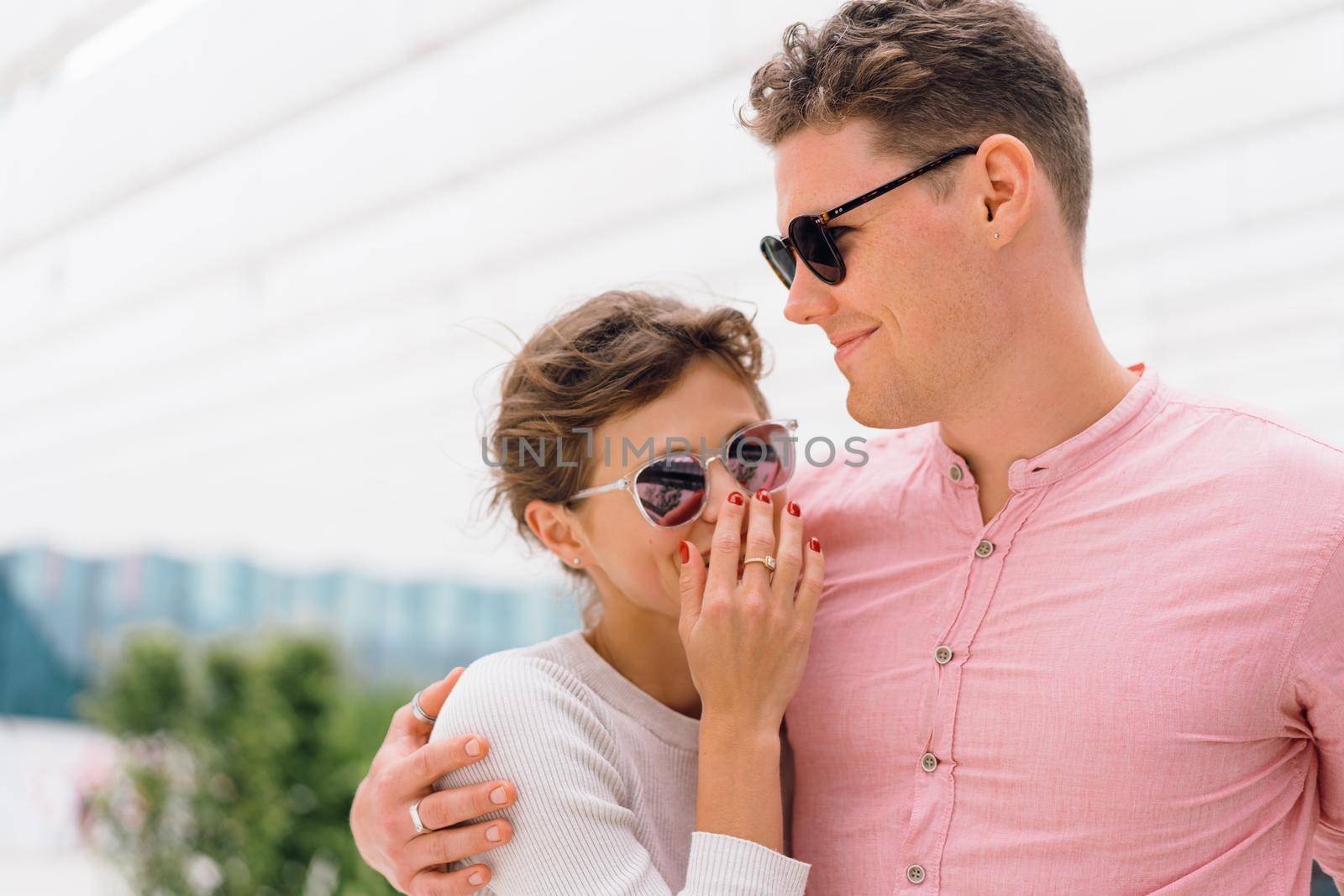 Smiling beautiful woman and her handsome boyfriend. Happy cheerful couple in sunglasses walking business district. Couple posing on the street modern building background