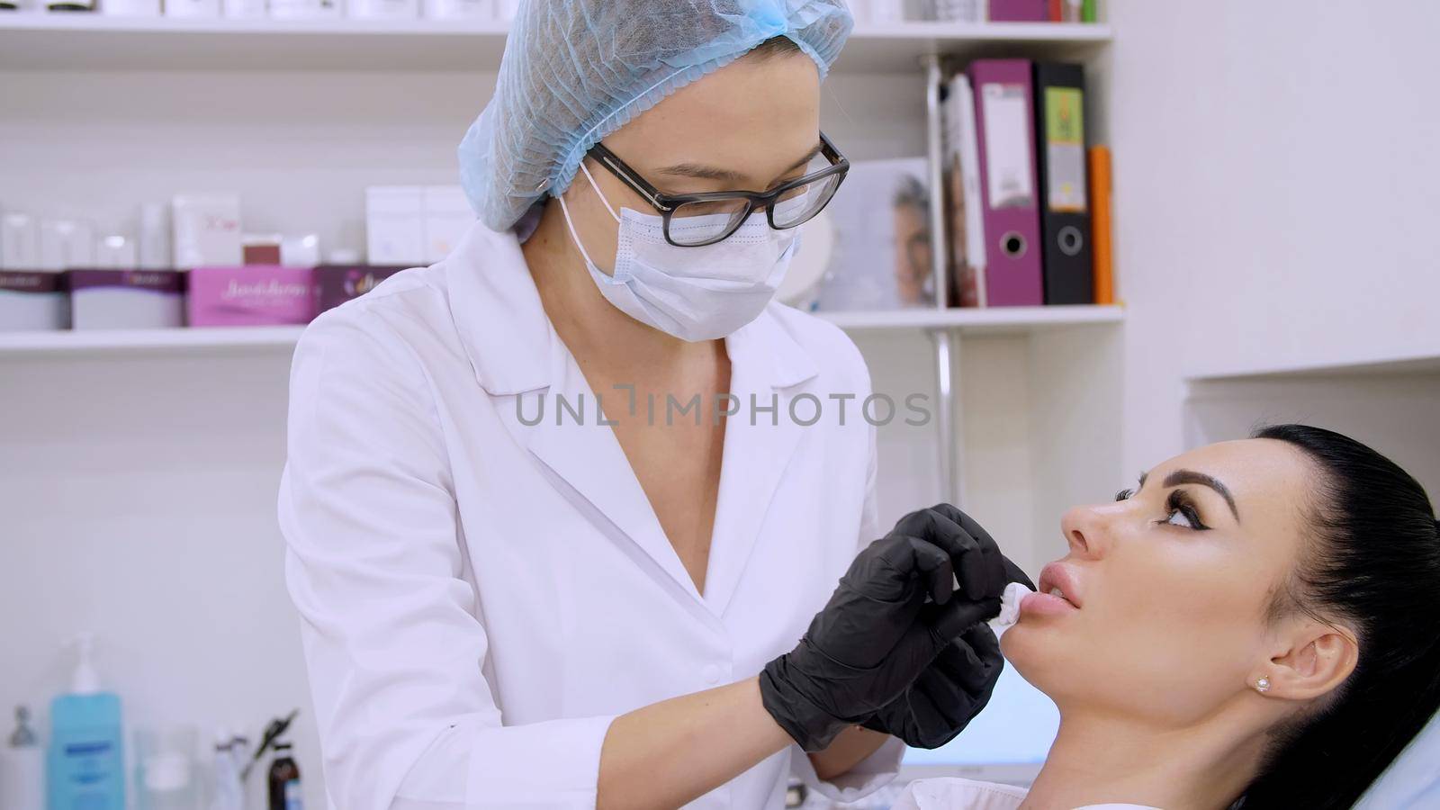 cosmetology room in the clinic, the doctor wipes patient lips with a sterile napkin, before injections of hyaluronic acid into lips, cleans the surface with an antiseptic. by djtreneryay