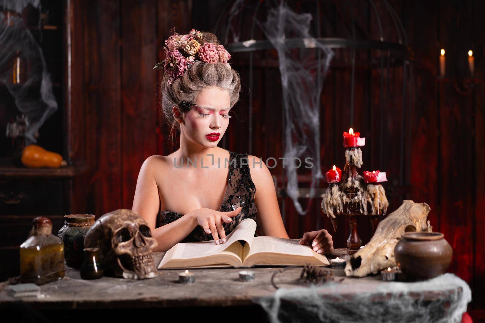 Portrait fortune teller woman reading future on magical book. Magic and divination. Young beautiful enchanted female witch sitting on the table waiting your desire. Scary Halloween atmosphere