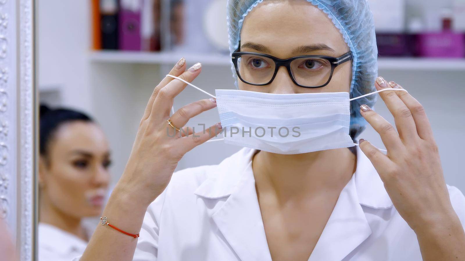 cosmetology room in the clinic, a female doctor wearing glasses, wearing a white uniform, dresses a medical cap and bandage. stands in front of a mirror. by djtreneryay