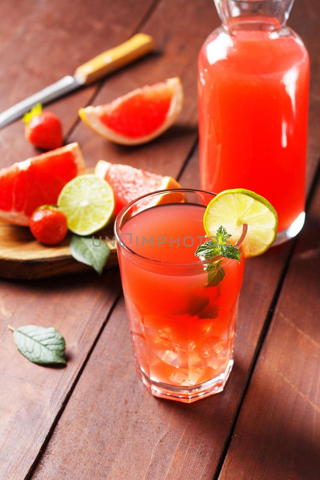 Fresh grapefruit juice in a glass with grapefruit pieces, lime and mint on a wooden background. vertical photo by lara29