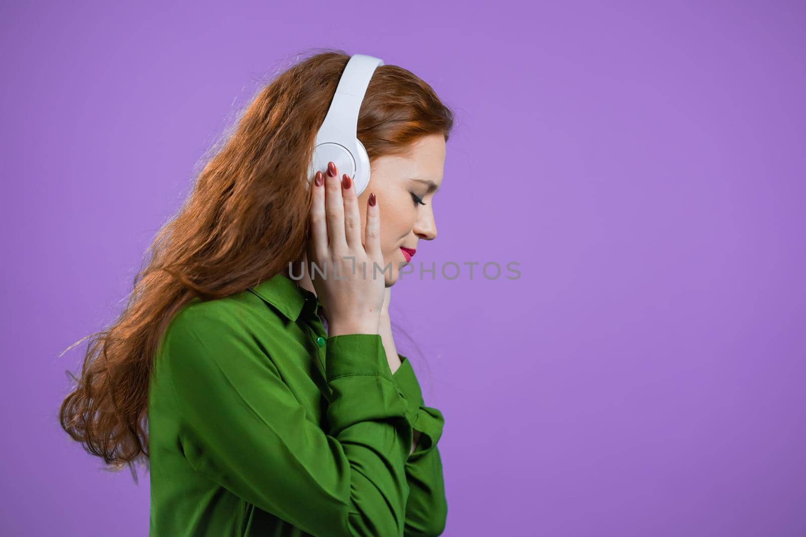 Pretty woman with white headphones on violet studio background. Cute girls portrait. Music, radio, happiness, freedom, youth concept. High quality