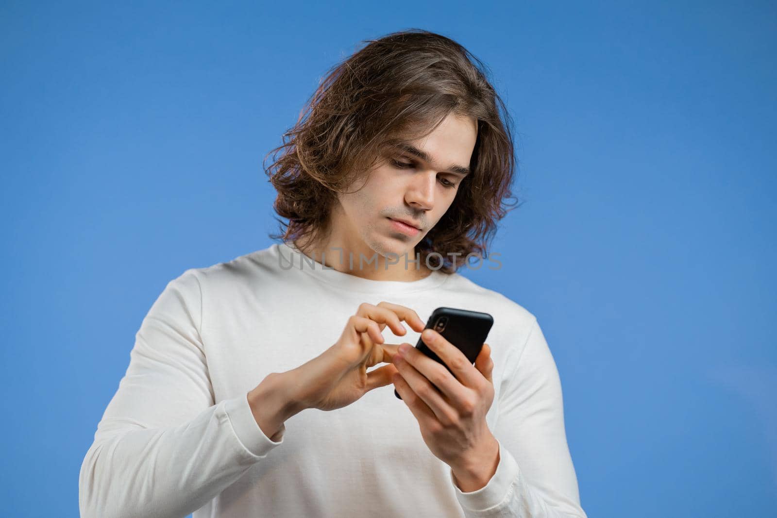 Handsome man using smartphone on blue studio wall. Modern technology - apps, social networks. High quality photo