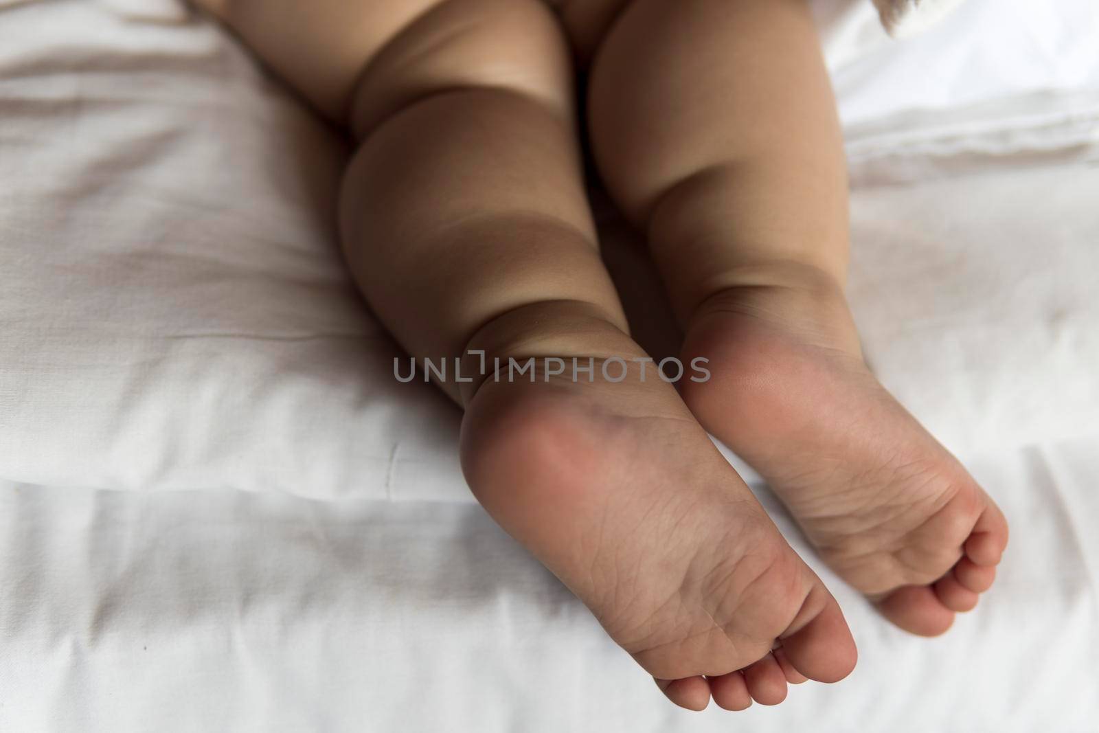 feet of toddler baby girl wearing diapers lying on white bed at home. plump legs of sleeping one year old caucasian child. kid sleeps in crib. home, comfort, childhood, care, love, sweet dream concept.