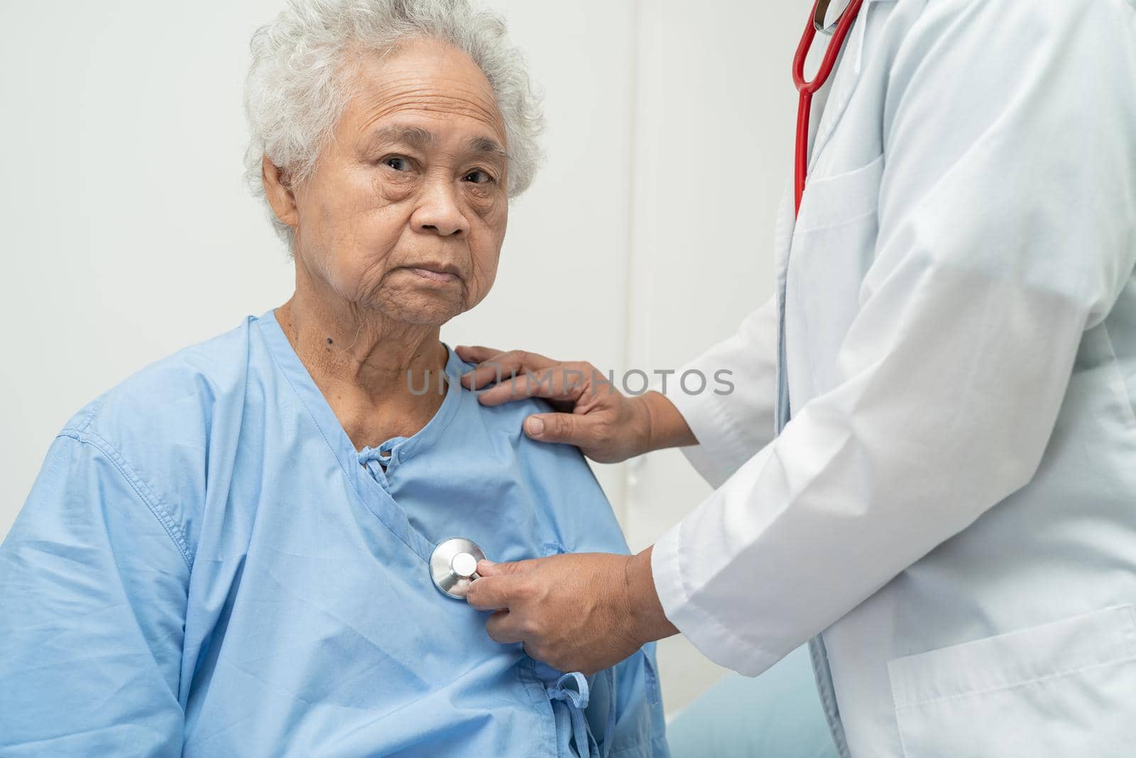 Doctor with stethoscope checking senior or elderly old lady woman patient while sitting on a bed in the nursing hospital ward, healthy strong medical concept. by pamai