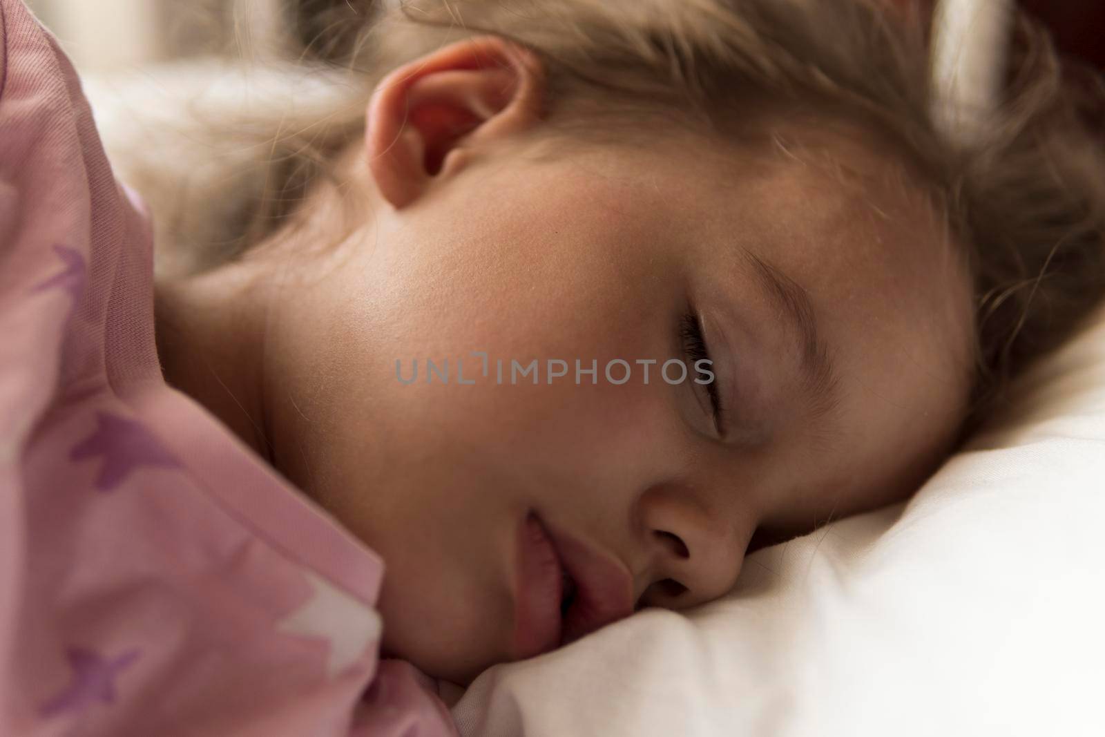 Cute cheerful little 3-4 years preschool baby girl kid sleeping sweetly in white crib during lunch rest time in pink pajama with pillow at home. Childhood, leisure, comfort, medicine, health concept.