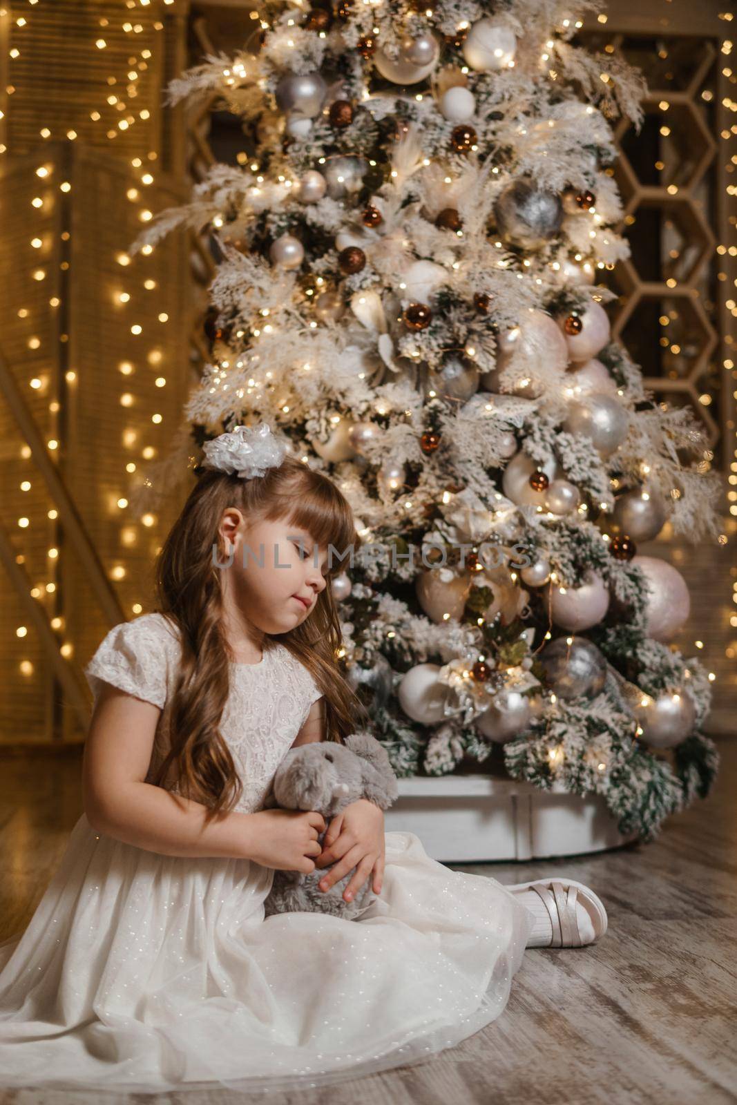 A girl in a festive light dress next to a Christmas tree, lights of garlands in the background. The concept of New Year holidays.