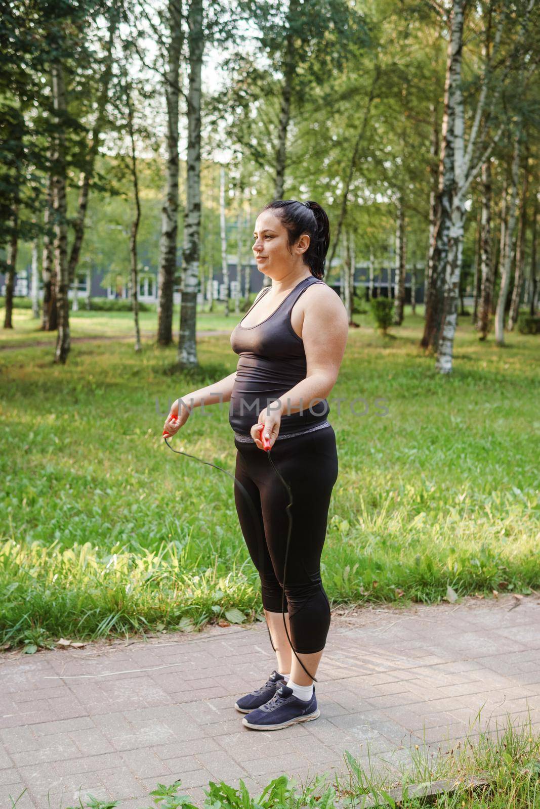 A charming brunette woman plus-size body positive practices sports in nature.