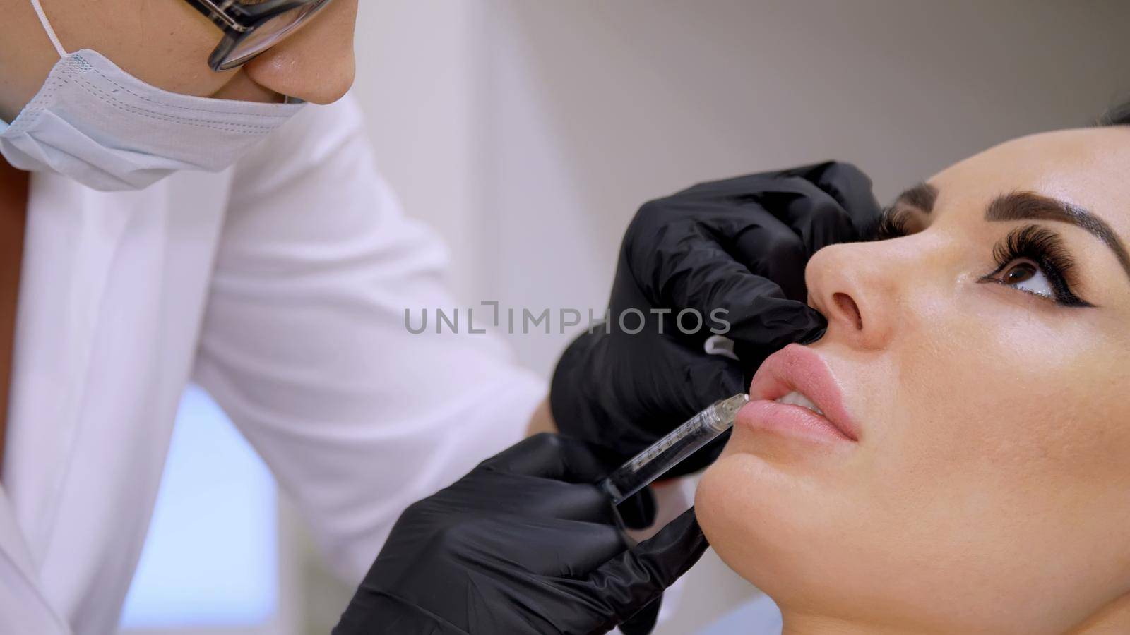 medical office, doctor in black sterile gloves, injecting hyaluronic acid into the patient lips. Procedure for increasing the volume of lips, correction of lips shape. High quality photo