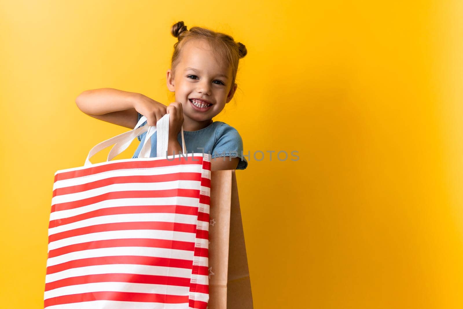 Portrait Caucasian Beautiful Happy Little Preschool Girl Smiling Cheerful And Holding Cardboard Bags Isolated On Orange Yellow Studio background. Happiness, Consumerism, Sale People shopping Concept.