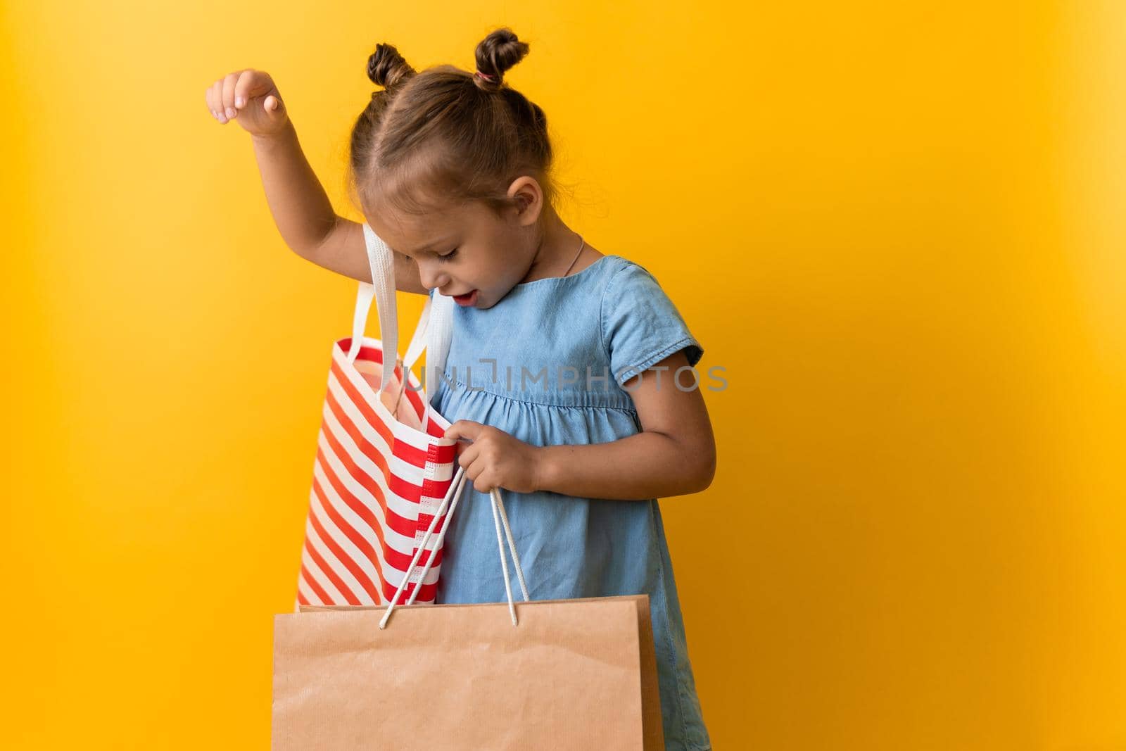 Portrait Caucasian Beautiful Happy Little Preschool Girl Smiling Cheerful And Holding Cardboard Bags Isolated On Orange Yellow Studio background. Happiness, Consumerism, Sale People shopping Concept.