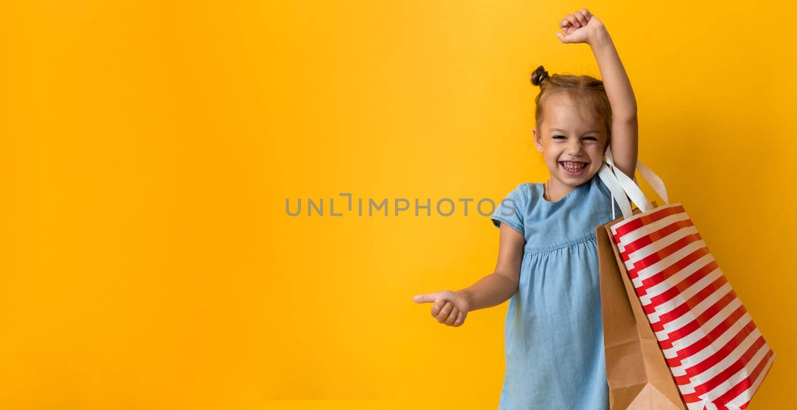 Banner Portrait Caucasian Beautiful Happy Little Preschool Girl Smiling Cheerful And Holding Cardboard Bags Thumb Up On Orange Yellow Background. Happiness, Consumerism, Sale People shopping Concept.