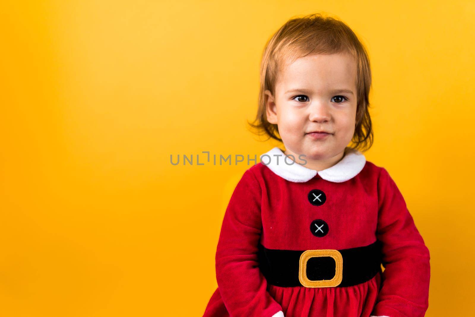 Banner Portraite Cute Happy Cheerful Chubby Baby Girl in Santa Suit Looking On Camera At Yellow Background. Child Play Christmas Scene Celebrating Birthday. Kid Have Fun Spend New Year Time Copy Space.