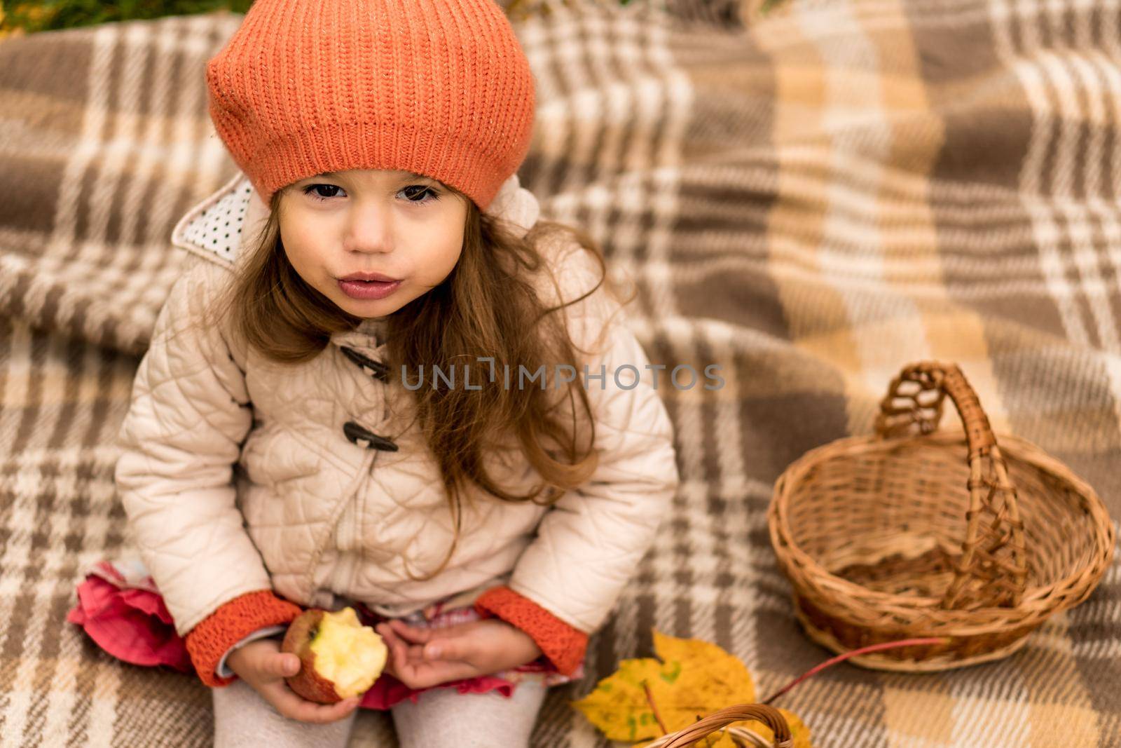 Close Up Portrait Of Little Cute Preschool Minor Girl In Orange Beret On Yellow Fallen Leaves Eats Red Apple Look At Camera Cold Weather In Fall Park. Childhood, Family, Motherhood, Autumn Concept.