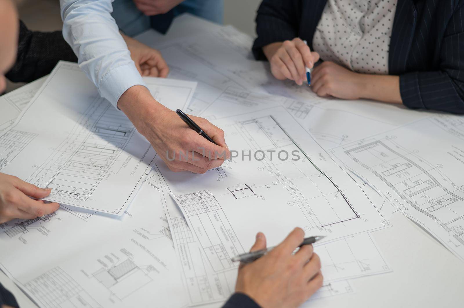 Close-up of the hands of four colleagues with blueprints on the table in the office. Brainstorming of engineers and architects