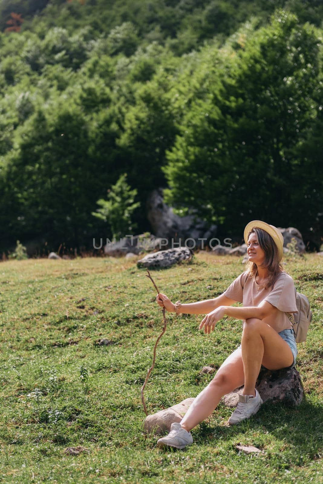Young woman sitting and relaxing on alpine mountain looking the cow eating a grass in the summer. Travel, Lifestyle Concept. Beautiful woman enjoys views of the alpine village in the Alps mountains. Happy tourist girl traveling to Europe by Andrii_Ko