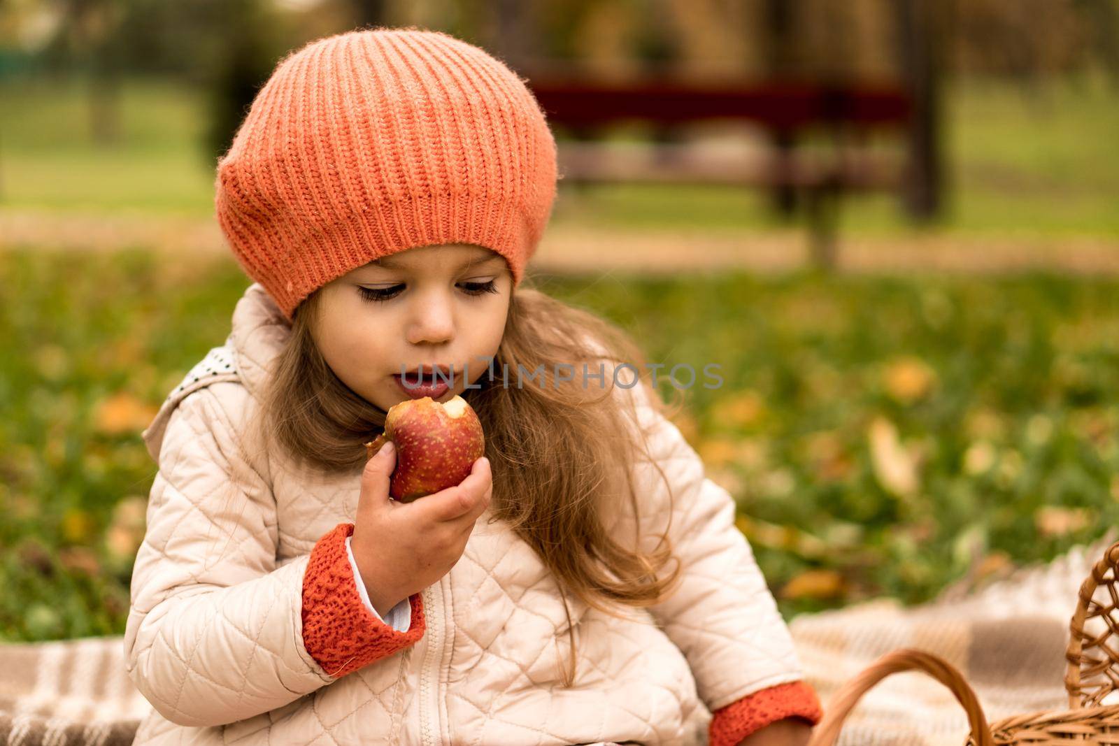 Close Up Portrait Of Little Cute Preschool Minor Girl In Orange Beret On Yellow Fallen Leaves Eats Red Apple Look At Camera Cold Weather In Fall Park. Childhood, Family, Motherhood, Autumn Concept.
