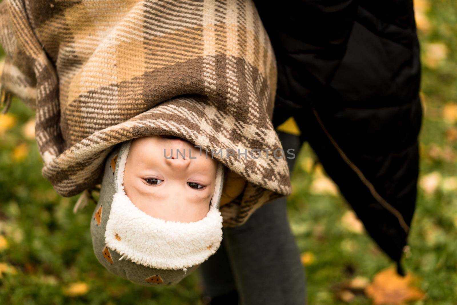 Young Woman Mom Holding Little Baby Boy Son Upside Down In Orange Plaid At Yellow Fallen Leaves Nice Smiling Look At Camera In Cold Weather In Fall Park. Childhood, Family, Motherhood, Autumn Concept by mytrykau
