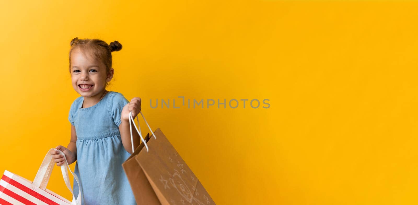Banner Portrait Caucasian Beautiful Happy Little Preschool Girl Smiling Cheerful Holding Cardboard Bags Leaving Shop On Orange Yellow Background. Happiness, Consumerism, Sale People shopping Concept.