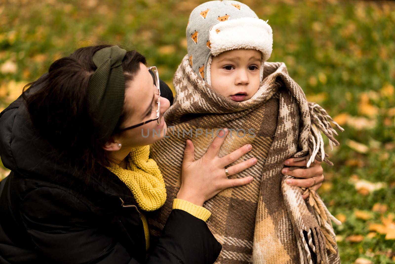 Young Woman Mom And Little Cute Preschool Minor Baby Boy In Orange Plaid At Yellow Fallen Leaves Nice Smiling Look At Camera In Cold Weather In Fall Park. Childhood, Family, Motherhood, Autumn Concept by mytrykau