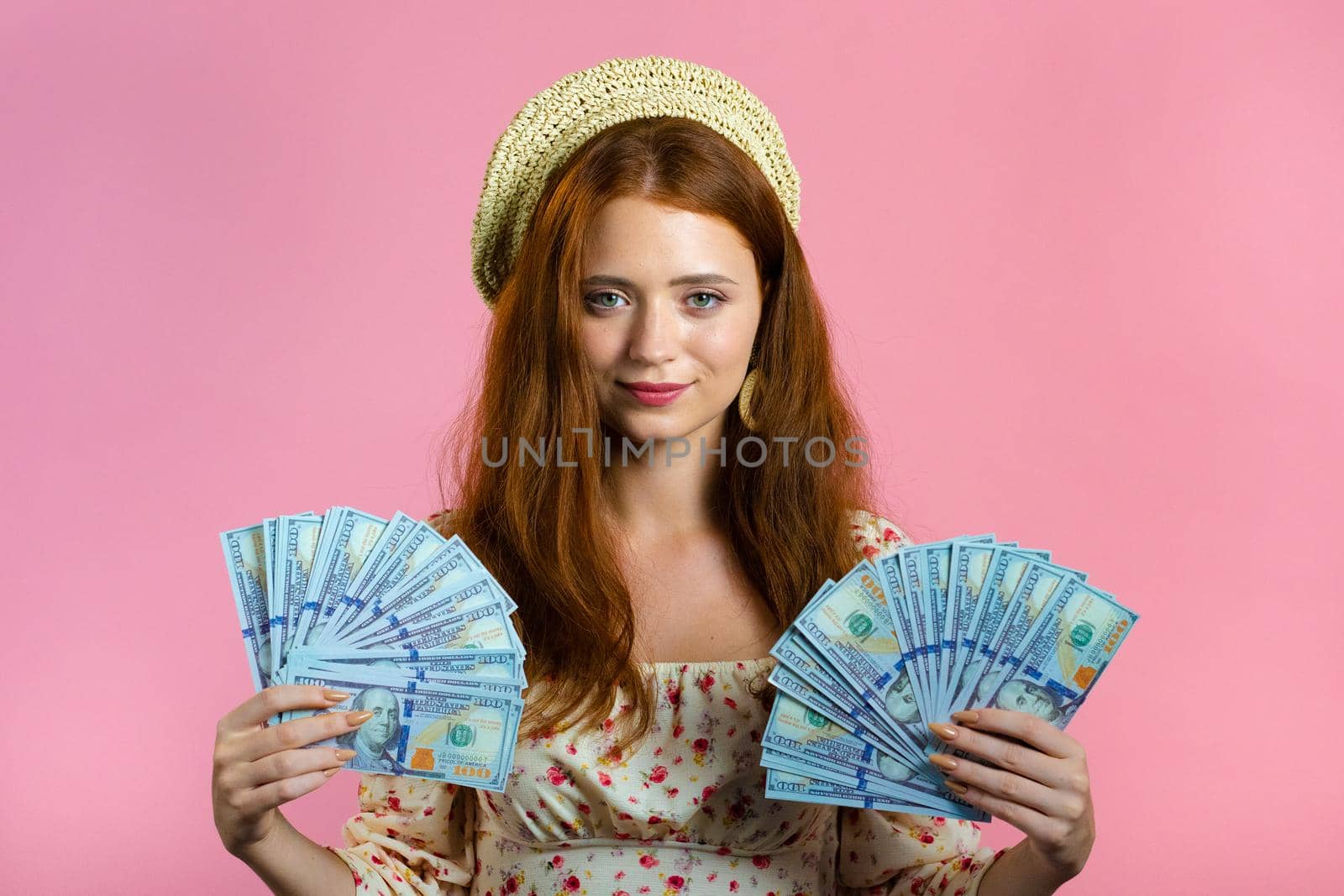 Amazed happy excited woman showing money - U.S. currency dollars banknotes on pink wall. Symbol of success, gain, victory