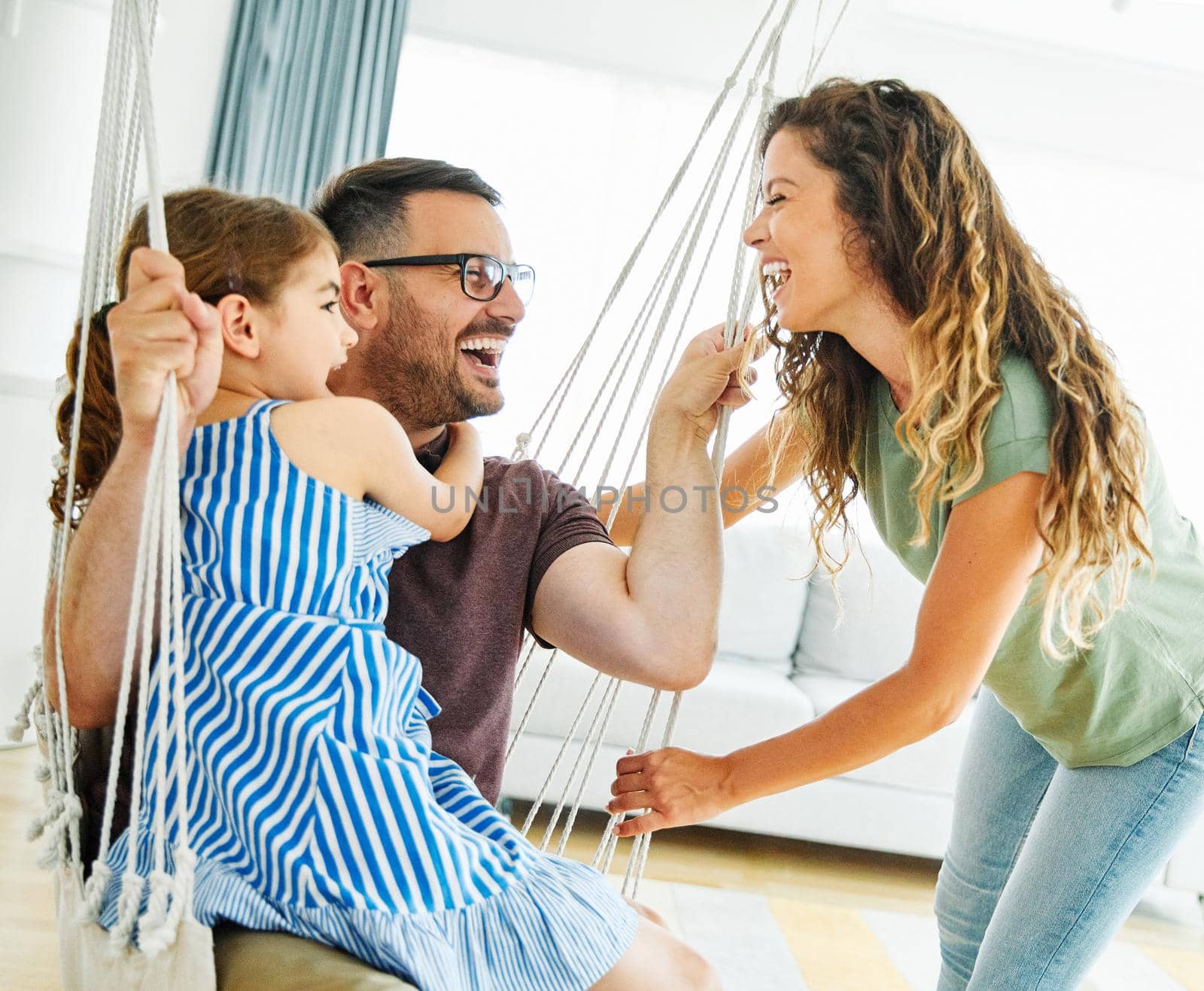 child daughter family happy mother father sofa playing fun together girl cheerful smiling home indoor swing by Picsfive