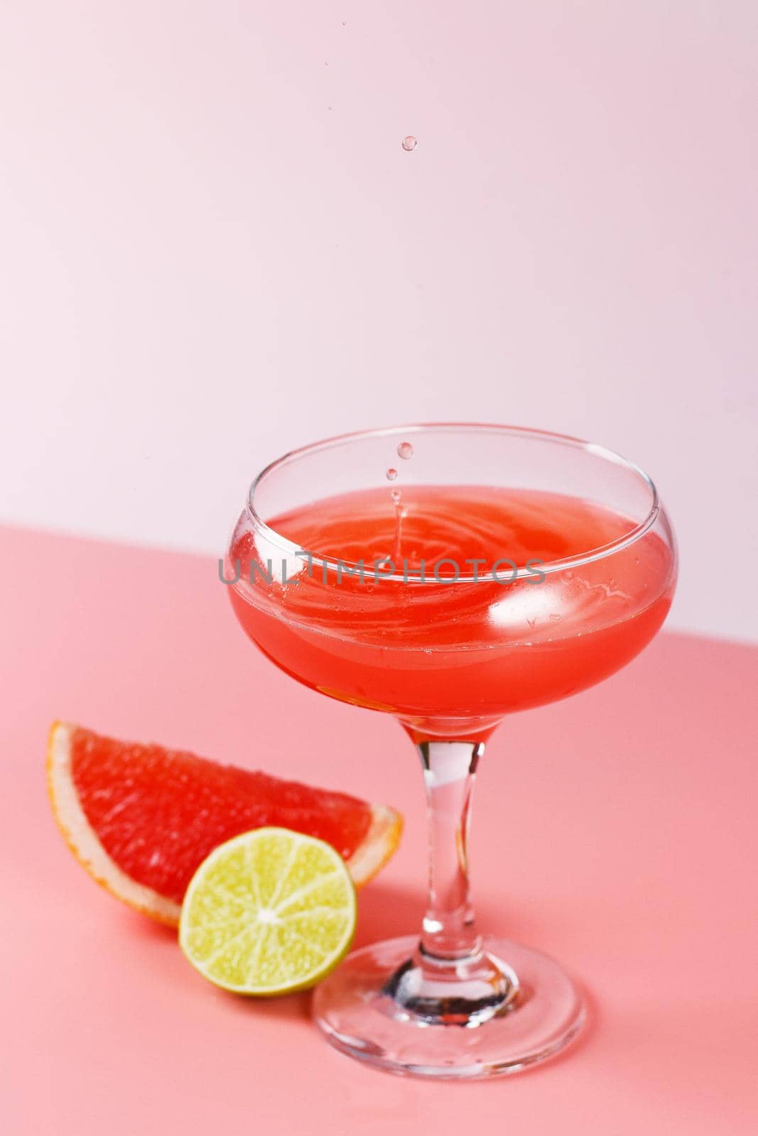 Fresh grapefruit juice with drops falling into a glass on a pink background with grapefruit slices and lime on a pink background. Copy space