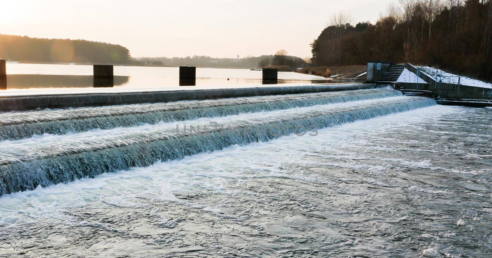 The river scenery. Cascade of water on the lake against the background of the sky with sunset.