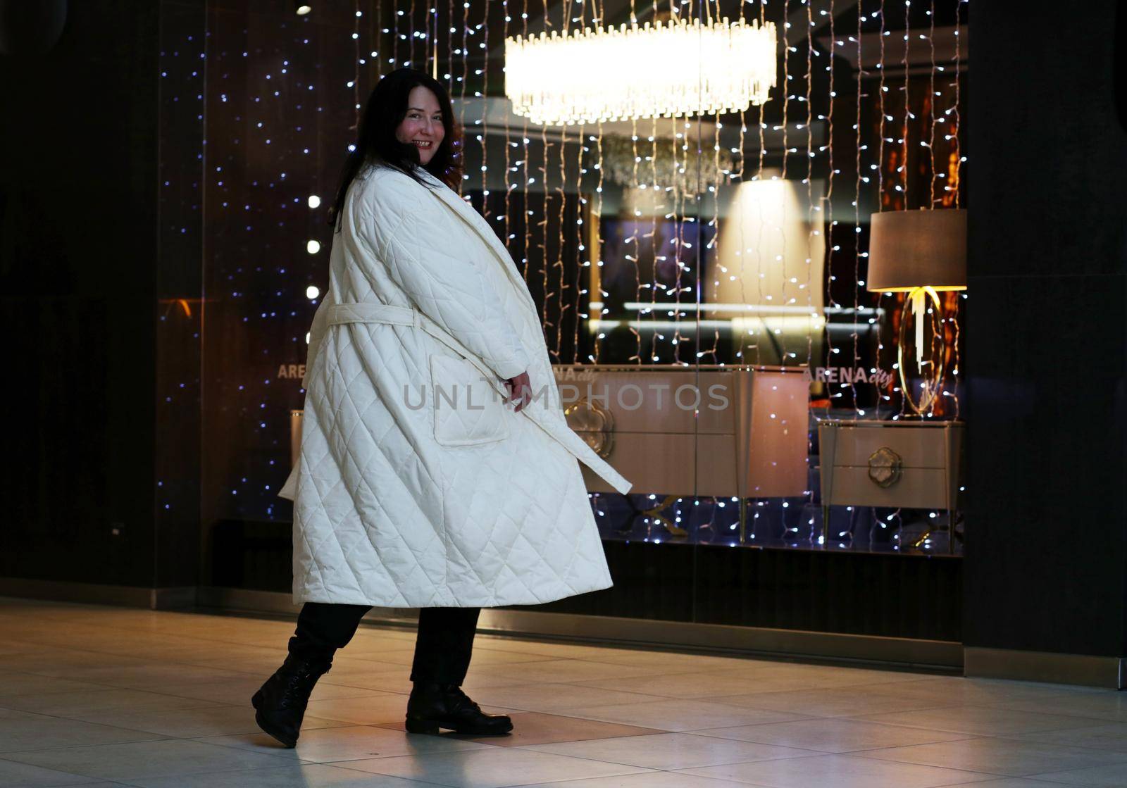 Brunette plus size in a full length white coat in a clothing store during her movement.