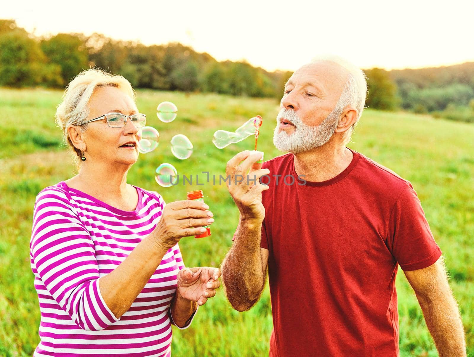 Happy active senior couple having fun blowing soap bubbles outdoors