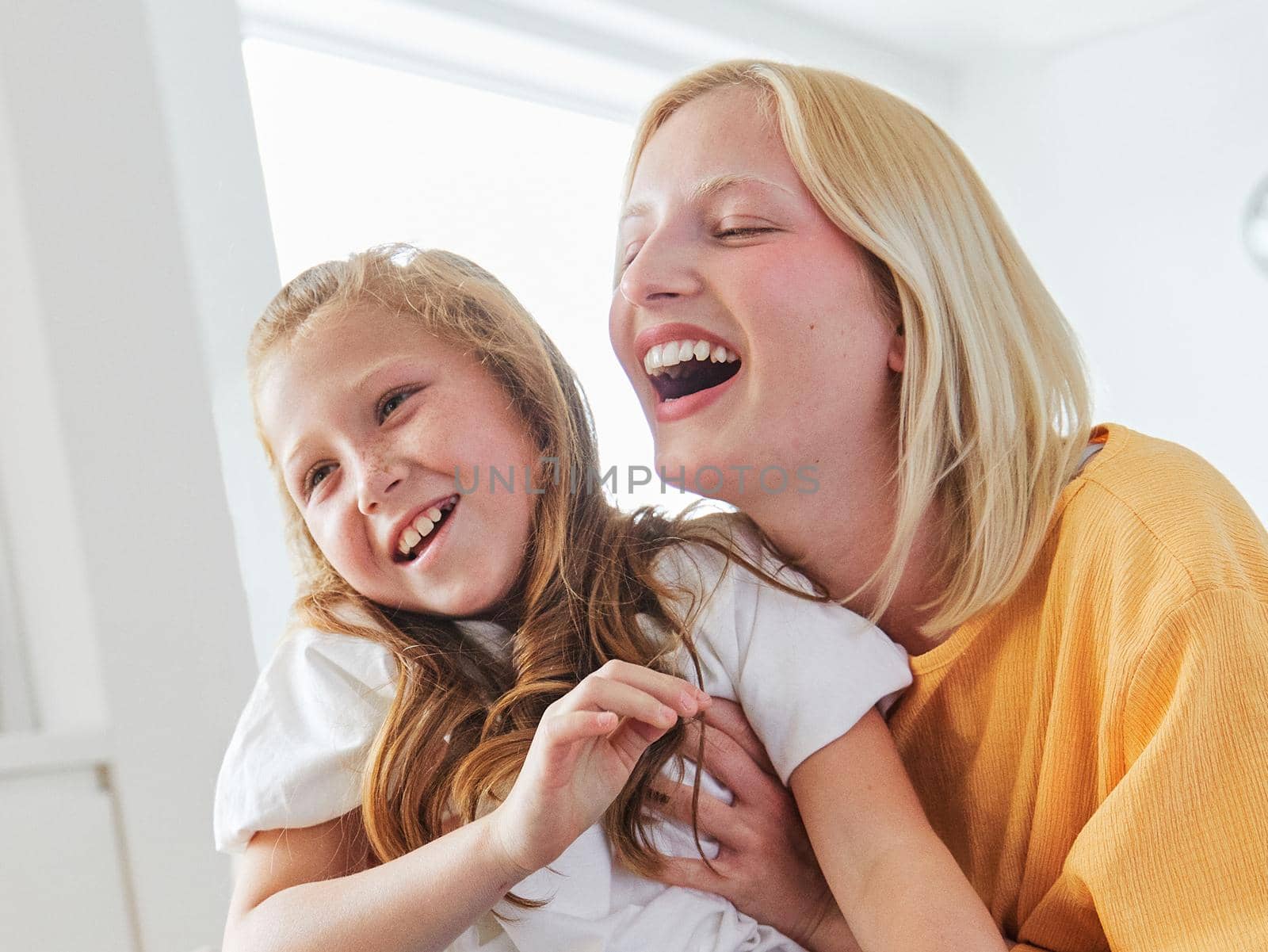 Portrait of two sisters or mother and daughter having fun together bonding sitting on sofa at home