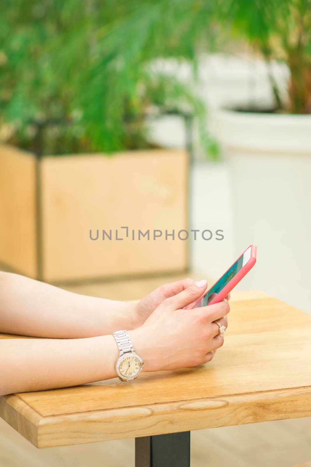 Hands of young white woman holding smartphone sitting at the table outdoors
