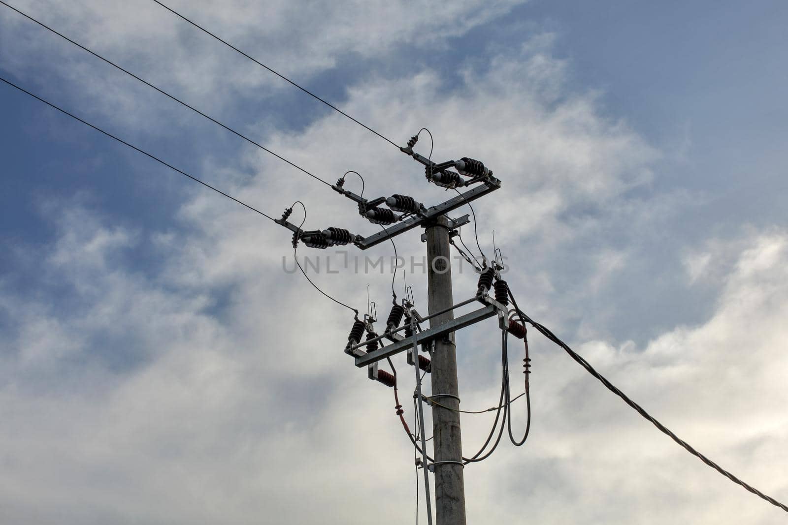 Small concrete pillar with power lines, sky with clouds in background.