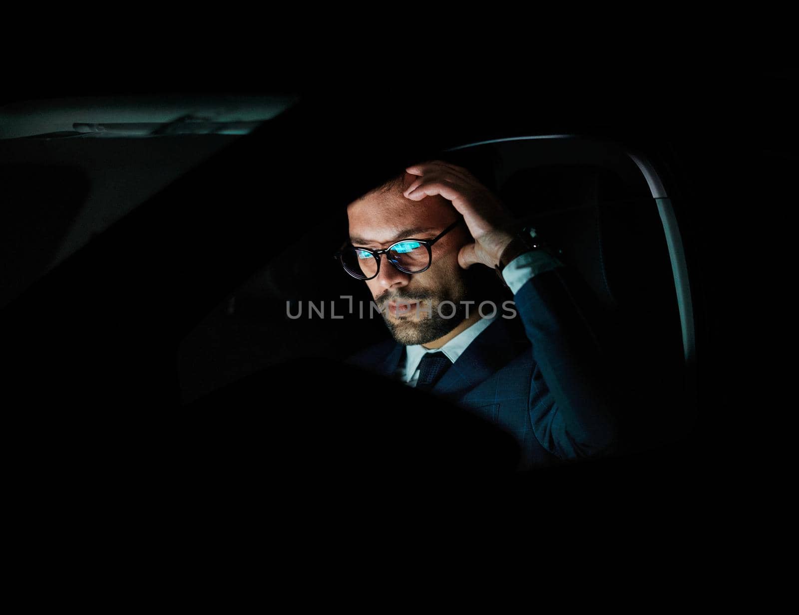 Portrait of a young businessman with tablet or laptop working late at night in office or looking at a device screen in car