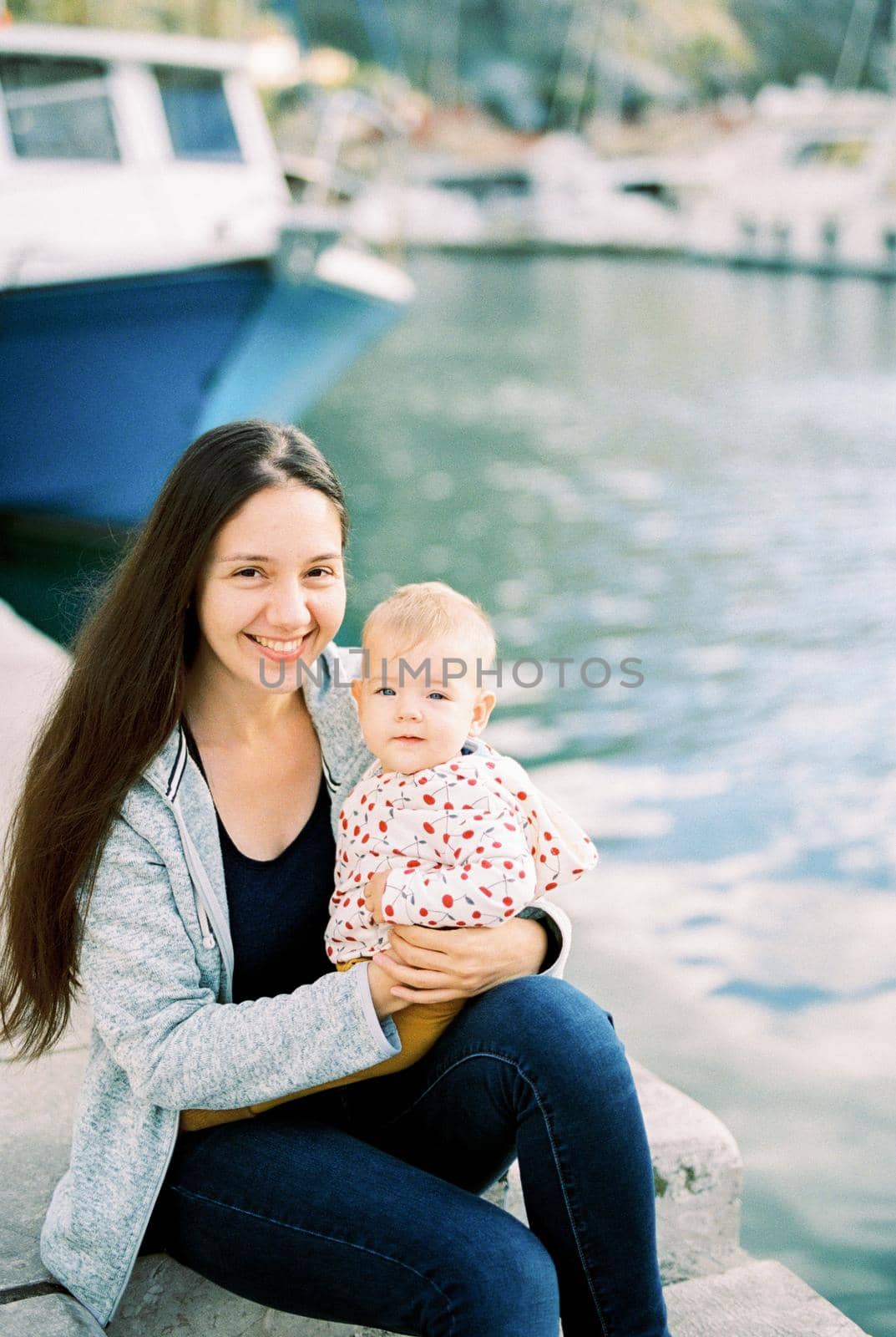 Smiling mother with a baby on her lap sits on the pier. High quality photo