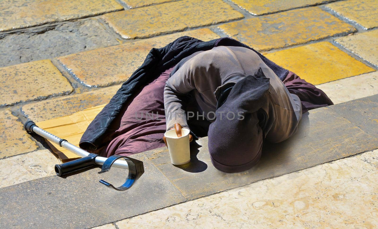 A woman in black clothes with a crutch begging for alms lying on the stairs in Europe