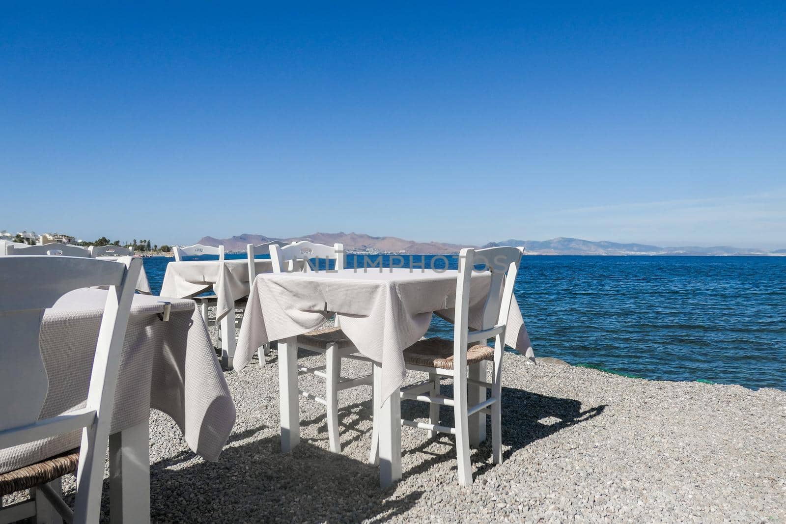 White restaurant tables on the beach in summer - travel, vacation and summer concept. The perfect lunch with a sea view