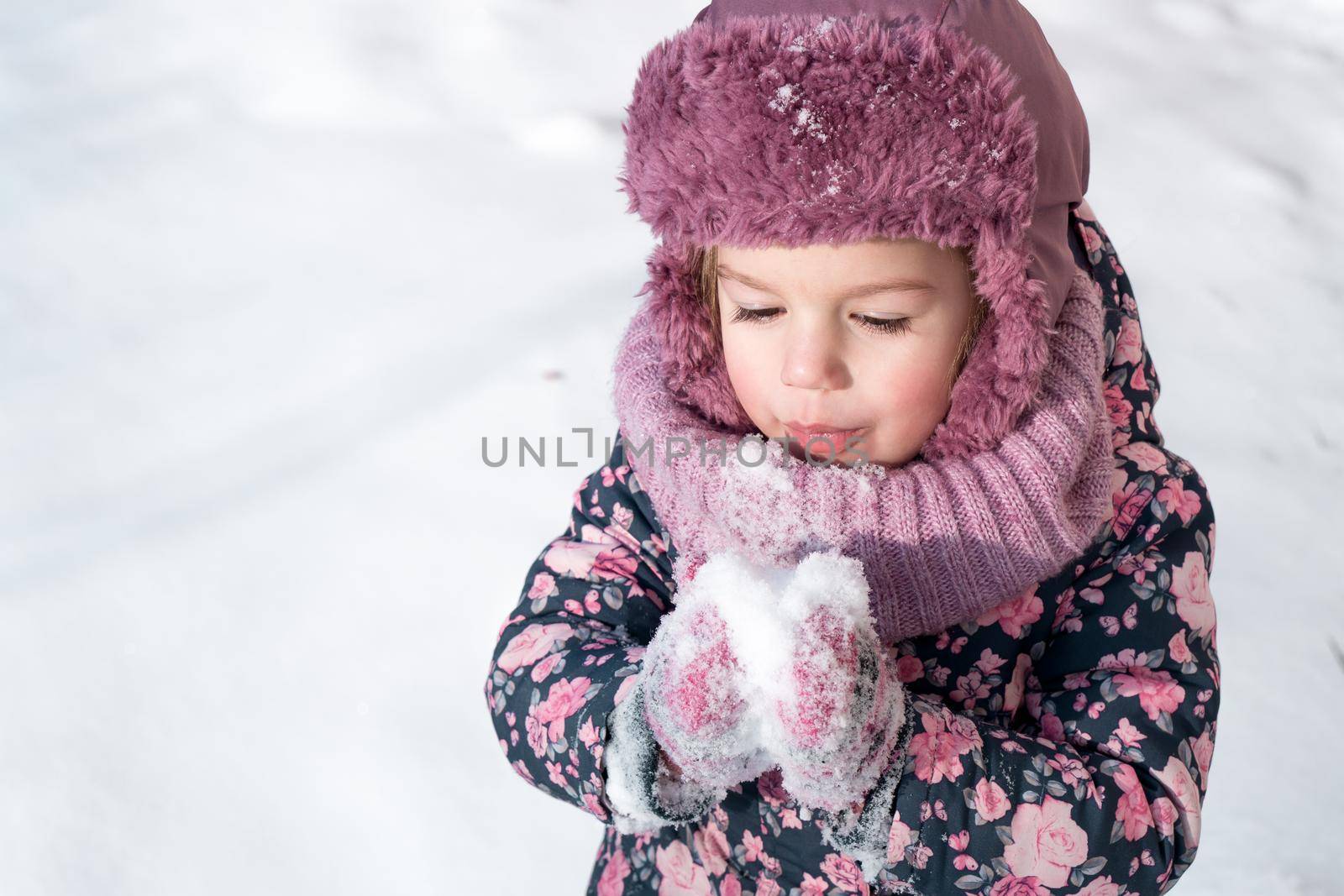 Winter, games, family, childhood concepts - close-up portrait authentic little preschool minor girl in pink hat warm clothes have fun smiles in cold frosty weather day. Funny kid blow on white snow.