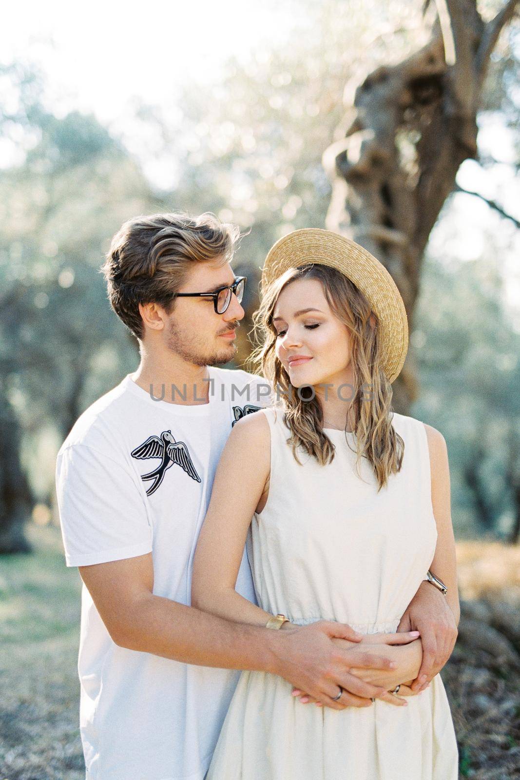 Man in glasses hugging woman in a straw hat from behind. High quality photo