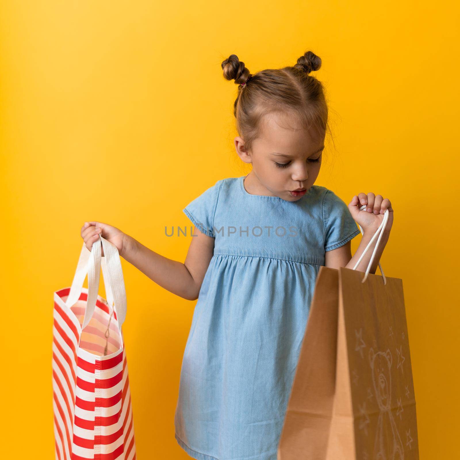 Squre Portrait Caucasian Beautiful Happy Little Preschool Girl Smiling Cheerful And Holding Cardboard Bags Isolated On Orange Yellow background. Happiness, Consumerism, Sale People shopping Concept by mytrykau
