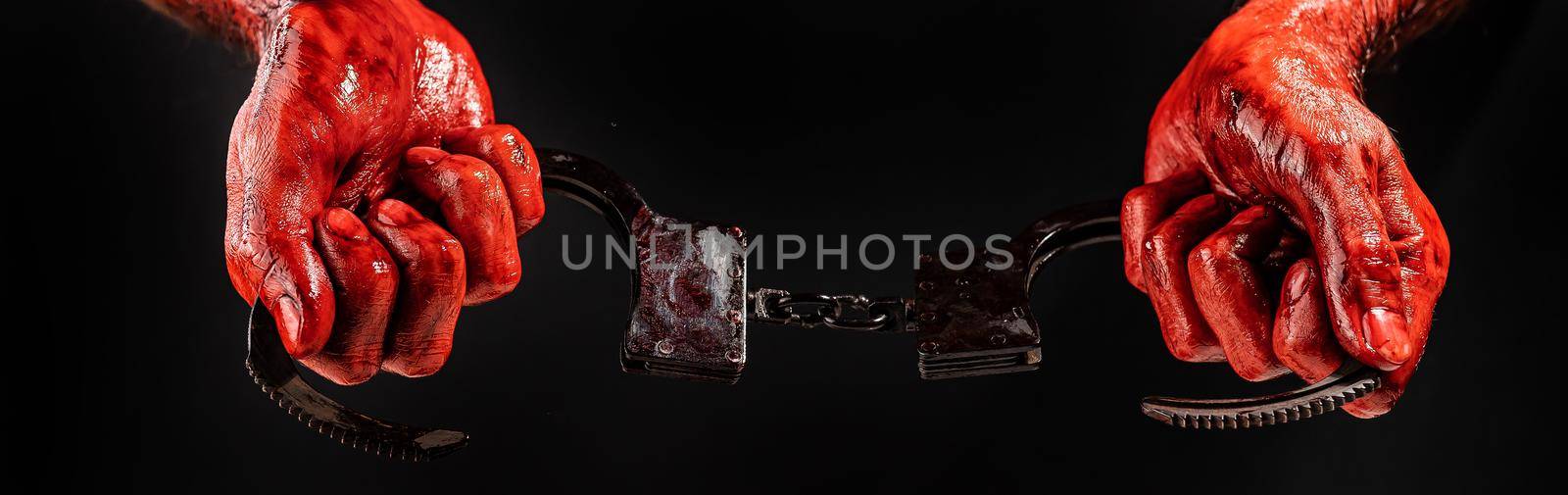 A man with bloody hands holds iron handcuffs