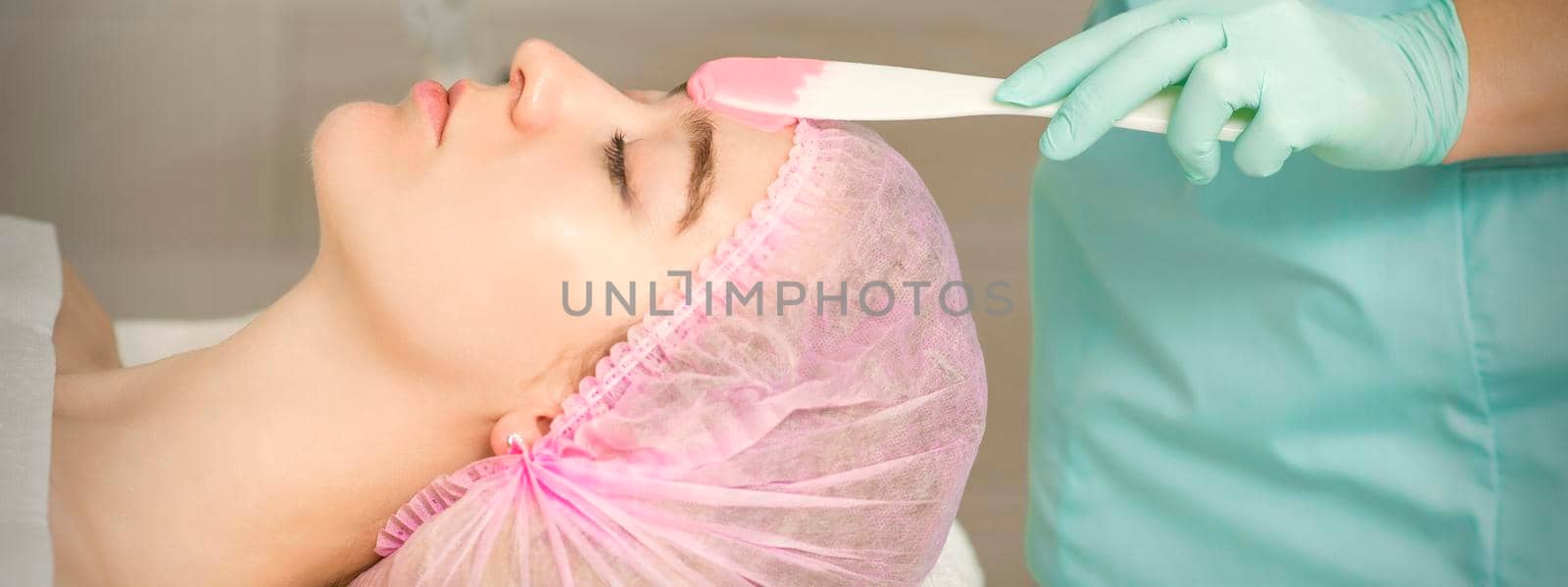 Close up of beautician's hand applying alginate mask on the face of the young caucasian woman in a beauty salon