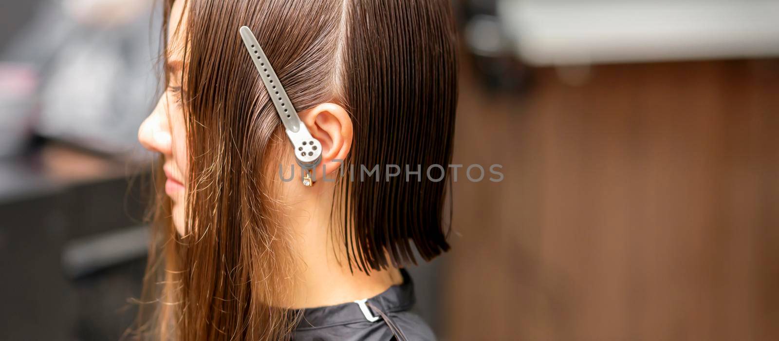 Close up side view of young brunette caucasian woman with split hair in sections in a hair salon