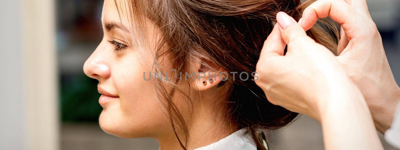Side view of hands of hair stylist styling hair of the beautiful young caucasian brunette woman in a beauty salon