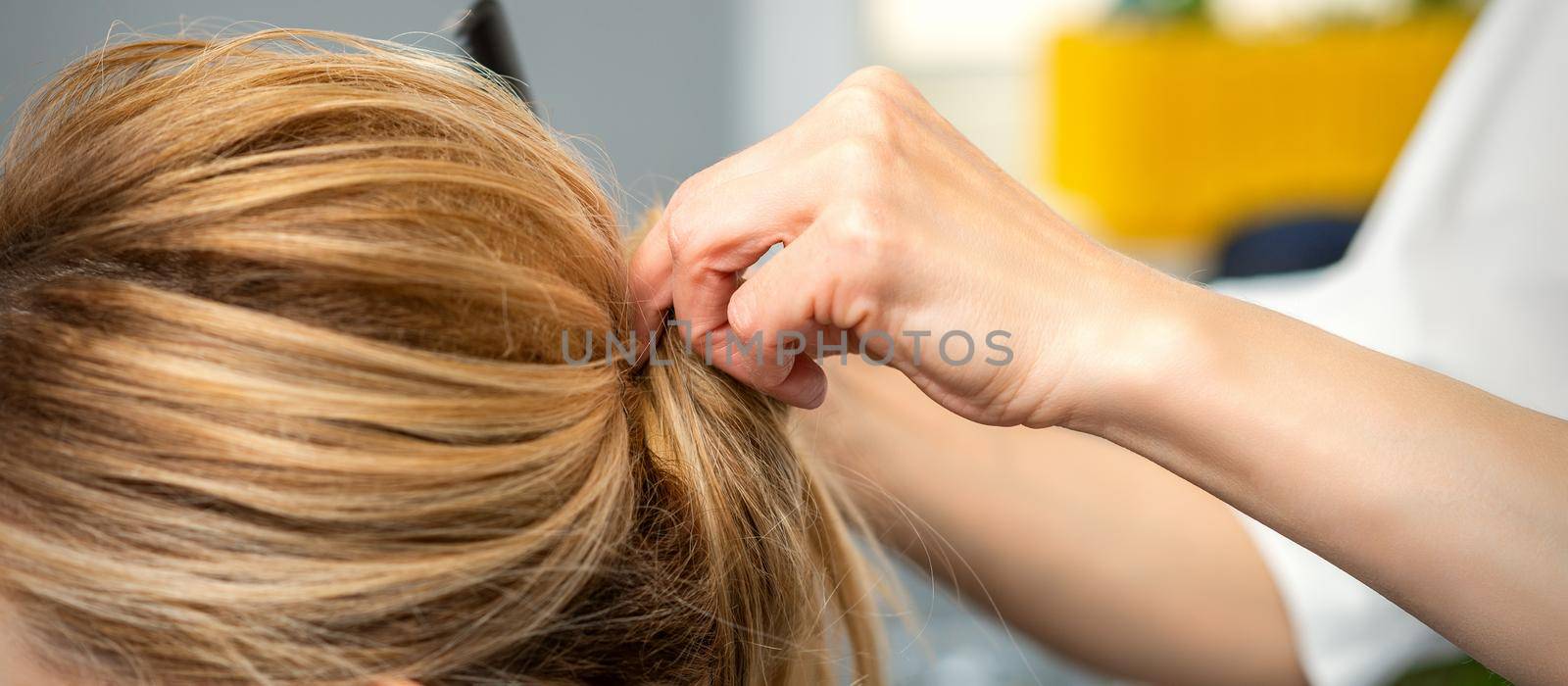 Close up of female hairdresser styling blonde hair of a young woman in a beauty salon