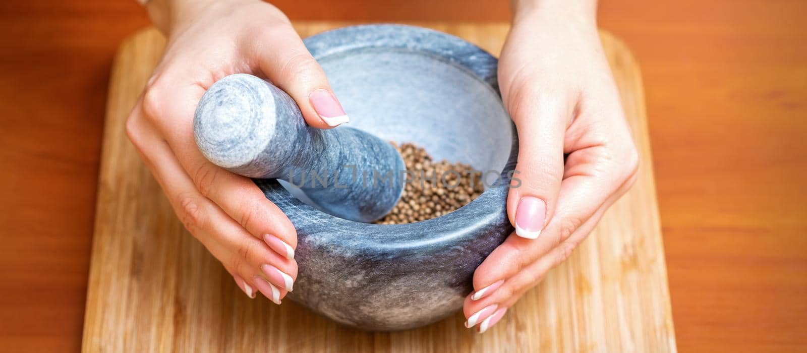 Female hands grind dry pepper spices in mortar on a wooden kitchen board