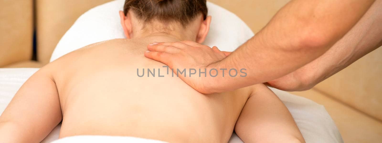 Hands of a masseur massaging back of a young adult woman in spa salon