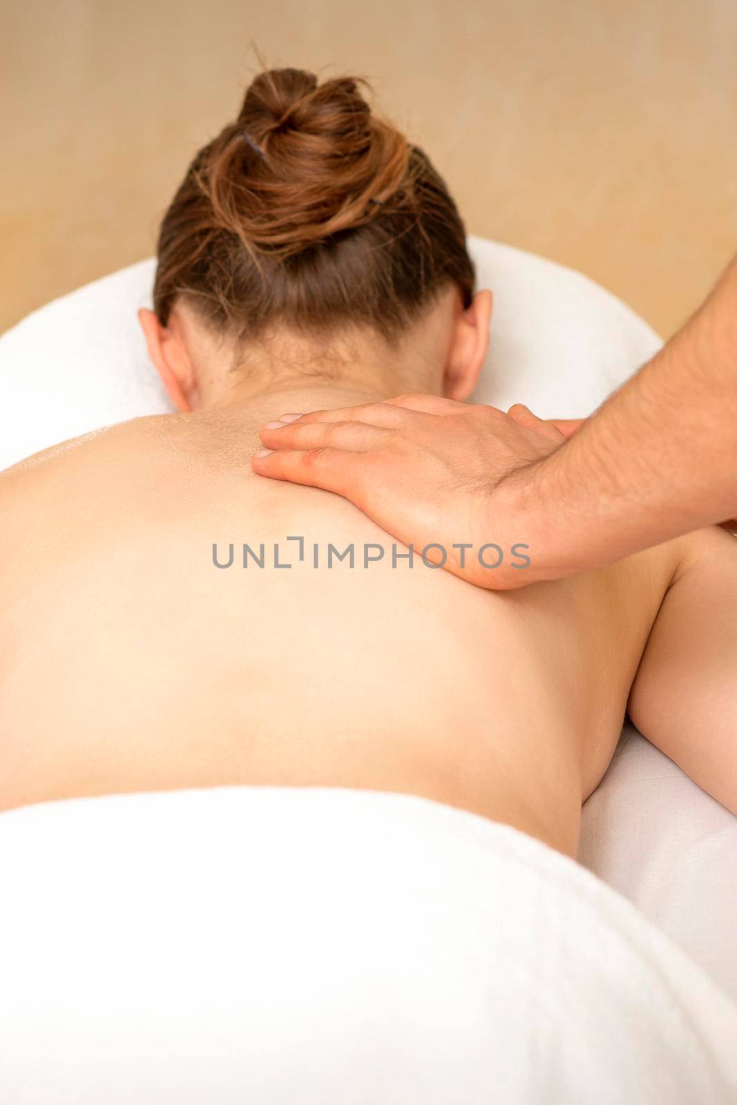 Hands of a masseur massaging back of a young adult woman in spa salon