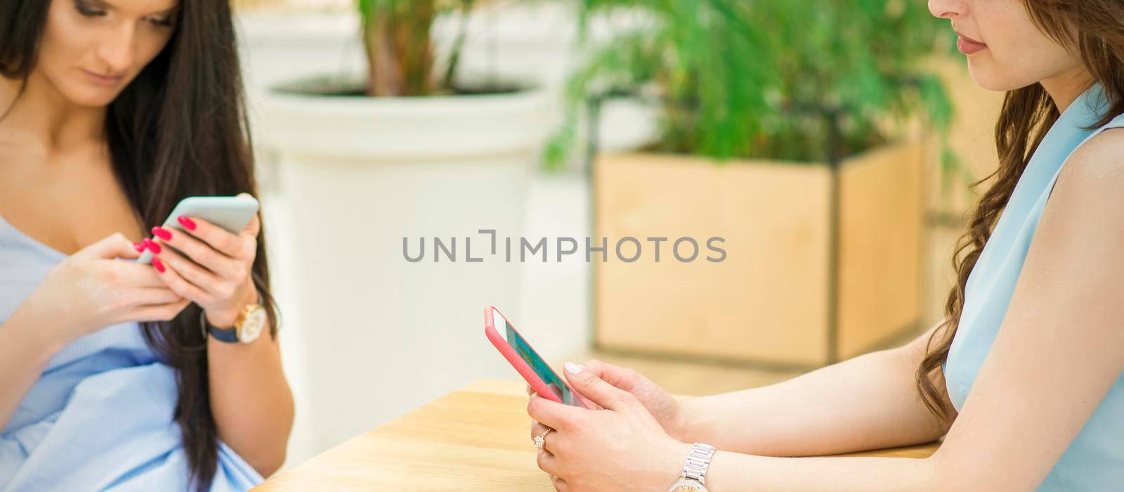 Two beautiful young caucasian women looking on smartphones sitting at the table outdoors