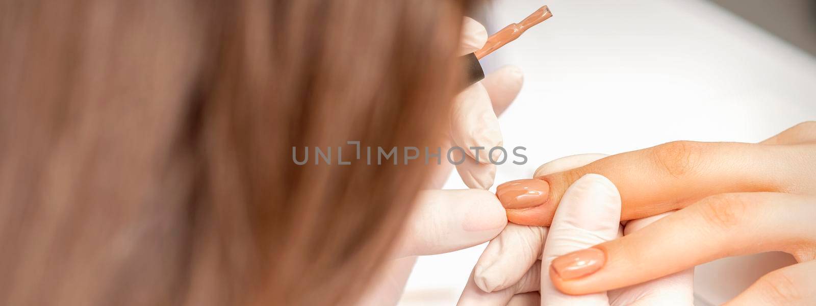 Manicurist applying beige nail polish on fingernails of a female client in a nail salon
